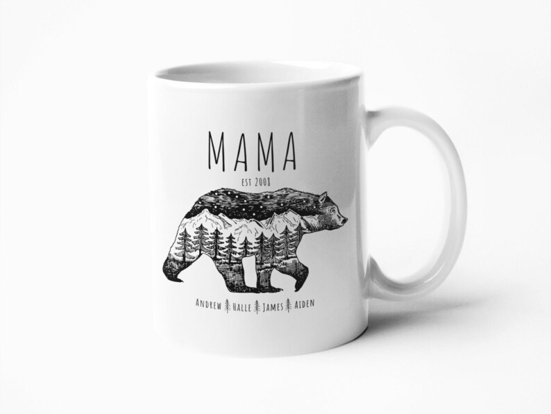 May include: White ceramic mug with a black and white illustration of a bear with mountains and trees inside its silhouette. The text "MAMA EST. 2000" is above the bear and the text "ANDREW HALLE JAMES AIDEN" is below the bear.
