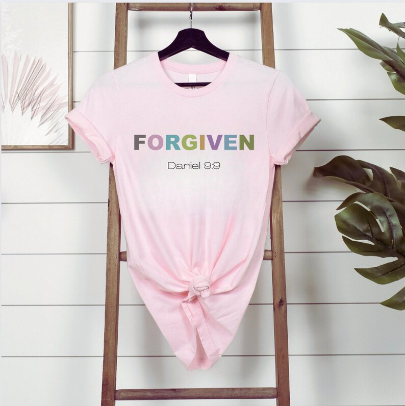 May include: A pink t-shirt with the word "FORGIVEN" in colorful letters and the text "Daniel 9:9" below it.