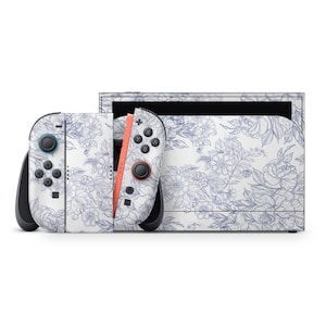 Könnte beinhalten: Eine weiße Nintendo Switch-Konsole und Controller sind mit einem blauen Blumenmuster verziert. Die Controller haben schwarze Knöpfe und eine korallenfarbene Schiene. Die Konsole ist weiß mit einem schwarzen Bildschirm.