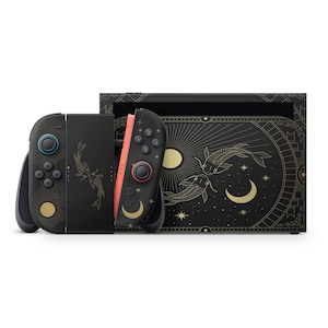 Könnte beinhalten: Schwarze Spielkonsole mit goldenen Koi-Fischen und Himmelsdesigns. Enthält zwei schwarze Controller mit türkisen und korallenfarbenen Akzenten sowie eine Dockingstation. Die Konsole hat ein goldenes Mond- und Sternenmuster.