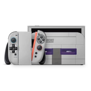 Könnte beinhalten: Eine graue Nintendo Switch-Konsole und Controller mit Retro-Design. Die Konsole hat einen Super Nintendo Entertainment System (SNES)-Stil mit lila und grauen Knöpfen. Die Controller sind grau mit blauen und korallenfarbenen Akzenten. Das Wort "CAPTURE" ist sichtbar.