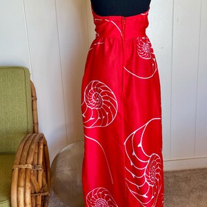 May include: A red halter-neck dress with a white nautilus shell pattern. The dress has a long, flowing skirt and a zipper closure down the back. The dress is displayed on a black mannequin.