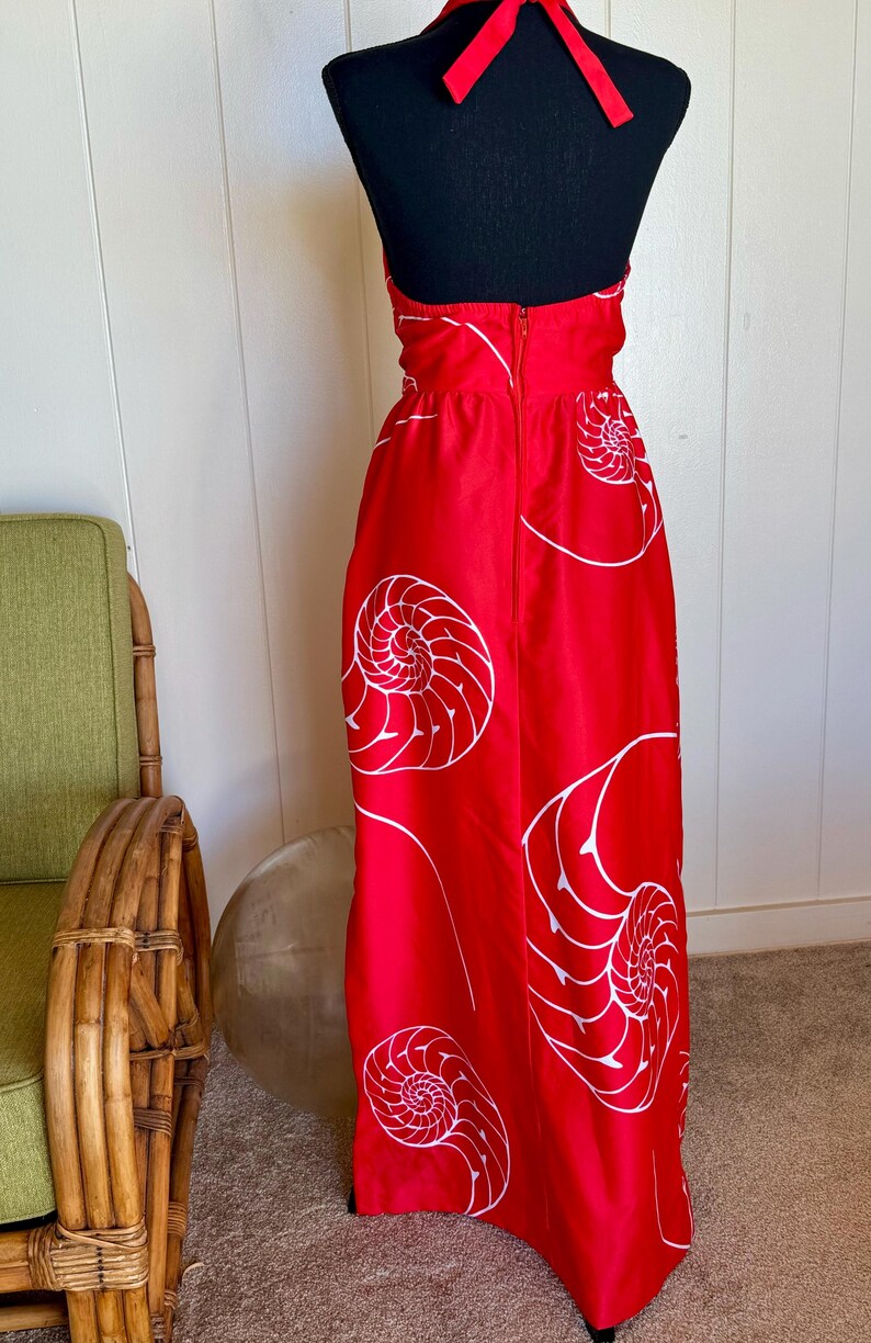 May include: A red halter-neck dress with a white nautilus shell pattern. The dress has a long, flowing skirt and a zipper closure down the back. The dress is displayed on a black mannequin.
