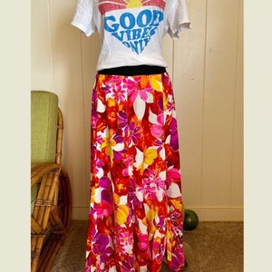 May include: A long, flowing skirt featuring a vibrant, multi-colored floral pattern in shades of red, pink, orange, and yellow against a white background. The skirt has a relaxed, loose fit and reaches down to the floor, showcasing a bold botanical print.
