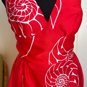 May include: A red halter dress with a white nautilus shell pattern. The dress features a V-neckline and a fitted waist. The white pattern is a repeating design of nautilus shells.