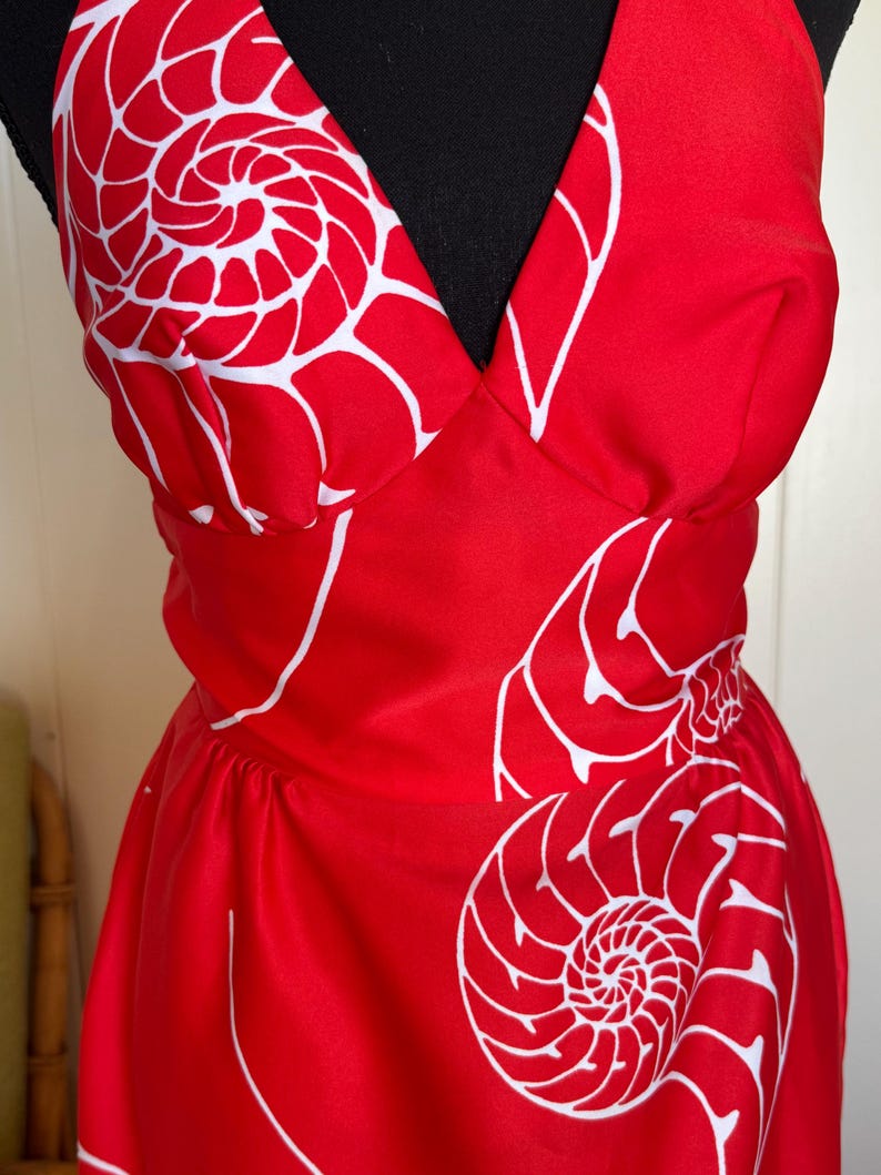 May include: A red halter dress with a white nautilus shell pattern. The dress features a V-neckline and a fitted waist. The white pattern is a repeating design of nautilus shells.