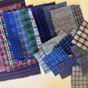 May include: A collection of rectangular fabric swatches featuring various plaid, checkered, and striped patterns in shades of blue, red, white, black, and grey. The textile pieces are arranged in an overlapping layout, displaying diverse woven textures.