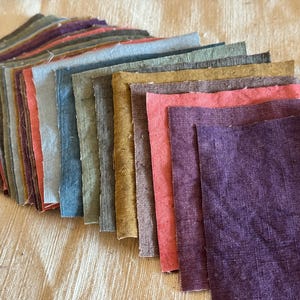 Peut inclure: Une collection d'échantillons de tissu rectangulaires disposés en éventail. Les pièces présentent une texture tissée visible et une palette de couleurs variée comprenant des nuances de violet, rose, jaune moutarde, vert olive, bleu et gris.