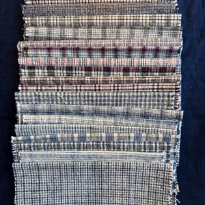 May include: A collection of fabric swatches in diverse plaid designs. The swatches display a variety of colours, including black, white, blue, and red. The fabrics have a textured look, with visible weave details. The swatches are arranged on a dark blue background.