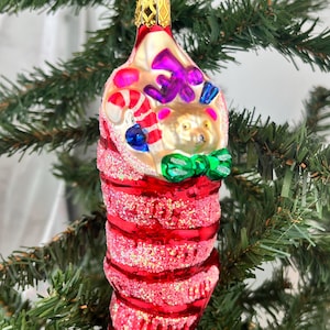 May include: A festive Christmas ornament shaped like a red stocking with glitter accents. The ornament features a teddy bear, candy canes, and a green bow. The top is gold with a star-shaped hanger.