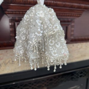 May include: A white beaded Christmas ornament with a ruffled design and silver accents.