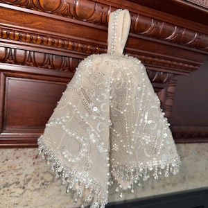 Puede incluir: Una media blanca de cuentas con un lazo para colgar. La media está decorada con lentejuelas y cuentas plateadas, y tiene un fleco de cuentas en la parte inferior.