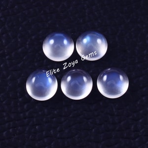 Könnte beinhalten: Sechs runde, weiße Mondstein-Cabochons mit einem blauen Schimmer. Die Steine sind in einem Halbkreis angeordnet, in der Mitte steht der Text "Elite Zoya Gems".