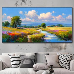 Può includere: Un dipinto di paesaggio incorniciato raffigura un prato vibrante con un ruscello sotto un cielo blu con soffici nuvole bianche. L'opera presenta fiori selvatici colorati, alberi e case distanti, creando una scena serena.