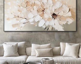 May include: Large floral painting with a black frame. The artwork features textured brushstrokes in shades of white, beige, and brown, creating a three-dimensional effect. The painting hangs above a cream-colored sectional sofa with matching pillows.