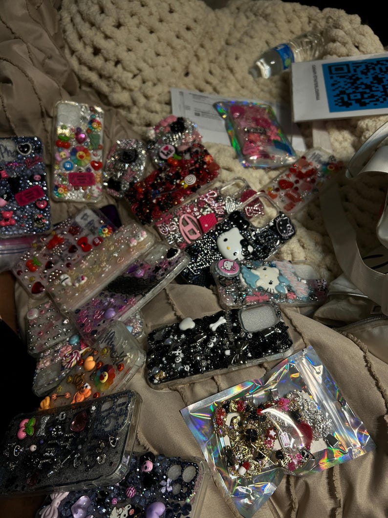 May include: A collection of decorative phone cases, featuring various designs with rhinestones, beads, and charms. The cases showcase a range of colors, including pink, black, and clear, with some cases featuring cartoon characters and floral patterns.