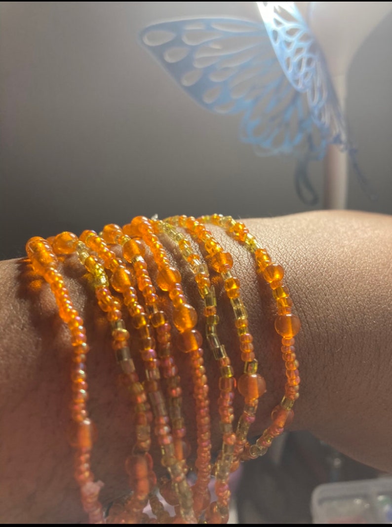 May include: A set of orange and yellow beaded bracelets. The bracelets are made of small, round beads and are stacked on top of each other.