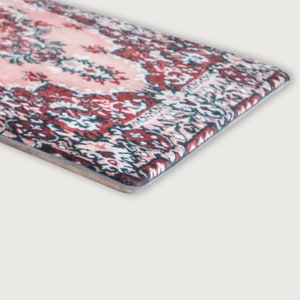 May include: A rectangular rug with a traditional Persian design. The rug features a central field of pale pink with intricate floral patterns in shades of red, navy, and white. The border is a darker red with a repeating geometric pattern.