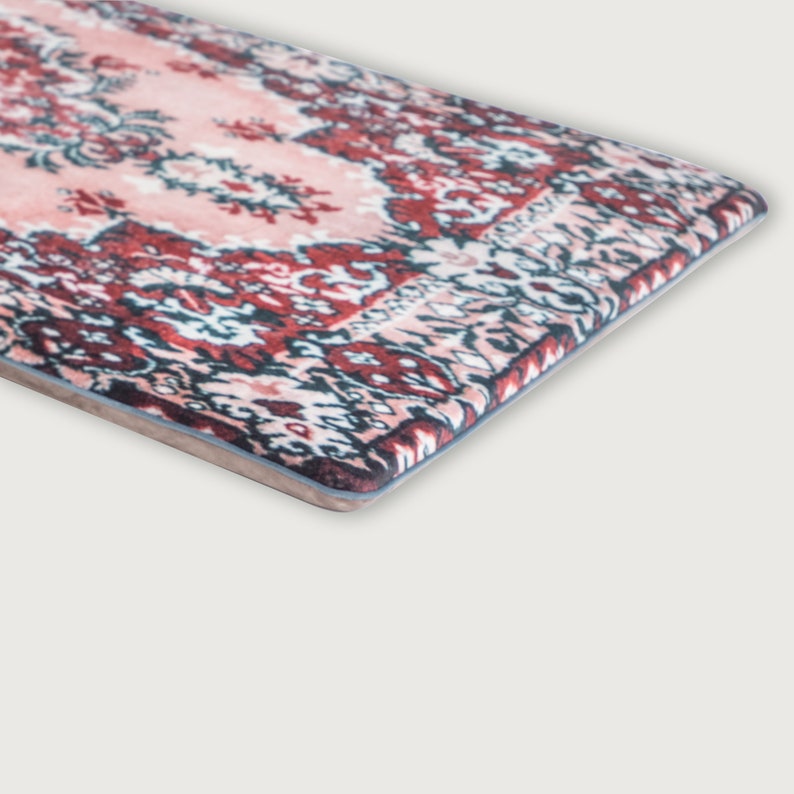 May include: A rectangular rug with a traditional Persian design. The rug features a central field of pale pink with intricate floral patterns in shades of red, navy, and white. The border is a darker red with a repeating geometric pattern.