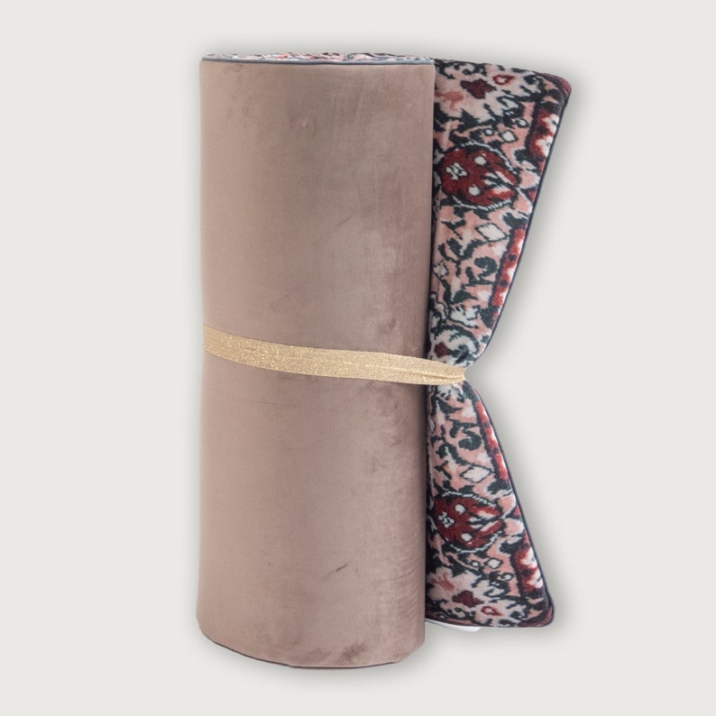 May include: Rolled-up area rug with a muted pink velvet exterior and a patterned interior. The rug is secured with a gold ribbon. The patterned section features a design with red, white, and green accents.