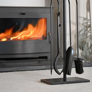 May include: Black metal fireplace tool set with a stand. The set includes a poker, tongs, shovel, and brush. The tools are hanging on a stand with a black base.