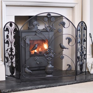 May include: Black metal fireplace screen with a decorative floral design and two birds. The screen is made of mesh and has three panels that fold out.