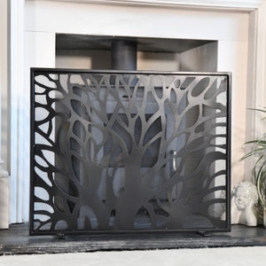 May include: Black metal fireplace screen with a tree-like design. The screen has a mesh backing and is designed to protect against sparks and embers.