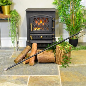 May include: A black metal fireplace poker with a silver tip, resting on a pile of logs in front of a black electric fireplace.