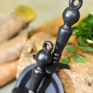 K&ouml;nnte beinhalten: Nahaufnahme von zwei schwarzen Metallkerzenhaltern mit Ringgriffen. Die Kerzenhalter haben ein verziertes Design und sind vor einem nat&uuml;rlichen Holzhintergrund platziert. Die Halter sind wahrscheinlich f&uuml;r Spitzkerzen.