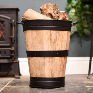 May include: A wooden log holder with black metal accents. The holder is shaped like a barrel and has a wide opening at the top. It is sitting on a tiled floor.