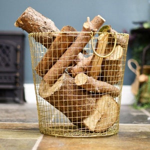 May include: A gold metal wire basket with a handle, filled with stacked pieces of firewood. The basket is sitting on a tiled floor.