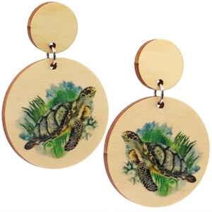 Può includere: Un paio di orecchini in legno con un design a tartaruga marina. Gli orecchini sono rotondi e hanno un colore legno chiaro. Le tartarughe sono dipinte in tonalità di verde, blu e marrone.