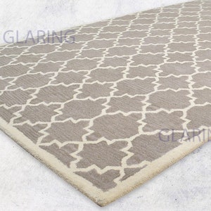 May include: A gray and white patterned rug with a white border. The rug has a geometric design with a repeating pattern of stars and diamonds.