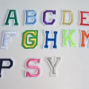 May include: A set of iron-on letters in various colours, including green, blue, purple, gold, red, white, light green, dark blue, orange, and pink. The letters are in uppercase and include A, B, C, D, E, F, G, H, K, M, P, S, and Y.