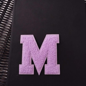 May include: A large, purple, fuzzy letter M on a black background.