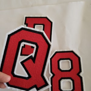 May include: Three red felt letters with black outlines and white backing. The letters are Q, 8, and D.
