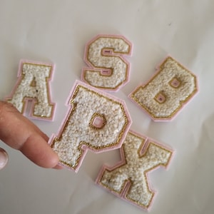 May include: Five felt letters in pink and gold, spelling out the word "SPAX". The letters are white with gold trim and pink backing.