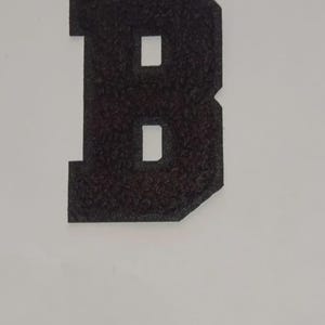 May include: Black felt letter B, in a varsity style font.