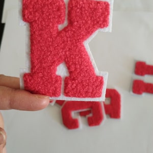 May include: Red felt letter K with a white outline. The letter is raised and has a fuzzy texture.