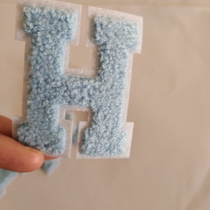 May include: A light blue felt letter H with white backing. The letter is cut out and ready to be ironed on.