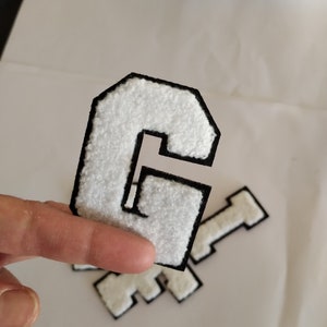 May include: White felt letter G with a black outline. The letter is thick and has a fuzzy texture.