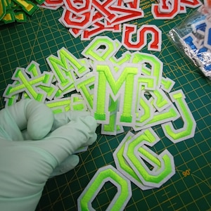 May include: A collection of green and white felt letter patches. The letters are in a variety of sizes and styles, including uppercase and lowercase. The patches are ideal for adding a personal touch to clothing, bags, or other accessories.