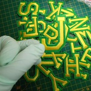 May include: A pile of green and gold felt letters, likely for a craft project or decoration. The letters are in various sizes and shapes, with a gold outline and a green interior.