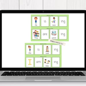 Pode incluir: Um laptop exibe tiras de frases educacionais com ilustrações e palavras como "Ele está chutando" e "Eles estão assistindo." A tela tem um fundo verde com retângulos brancos. Uma planta está à direita.