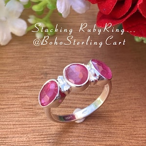 Peut inclure: Une bague en argent avec trois pierres de rubis roses. La bague est posée sur une surface en bois. Le texte "Stacking Ruby Ring... @BohoSterlingCart" est visible sur l'image.