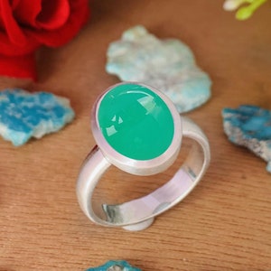 以下が含まれることがあります： ベゼルセッティングにセットされた明るい緑色の楕円形の宝石が付いたシルバーリングです。