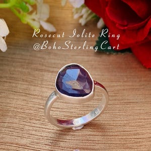 May include: A silver ring with a purple iolite gemstone. The gemstone is a rose cut and has a teardrop shape. The ring is on a wooden surface.  Rosecut Iolite Ring @boho_sterlingcart