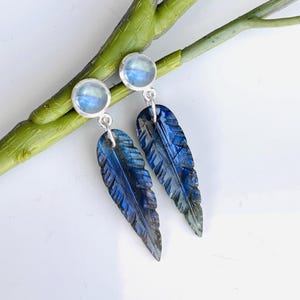 Op de afbeelding: Een paar oorhangers met gegraveerde blauwe labradorit verencharms en ronde maansteen accenten.