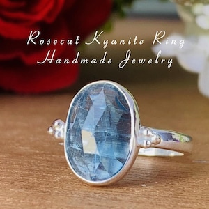 Op de afbeelding: Een zilveren ring met een blauwe kyanite edelsteen. De ring is gezet met een roos geslepen edelsteen en heeft een eenvoudige band. De tekst "Rosecut Kyanite Ring Handmade Jewelry" is zichtbaar in de afbeelding.