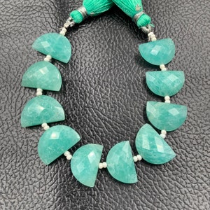 Puede incluir: Un collar de cuentas de piedra preciosa Amazonita. Las cuentas son de color verde azulado claro, cortadas en forma de media luna y facetadas. El collar est&aacute; ensartado en un cord&oacute;n blanco y terminado con una borla verde.